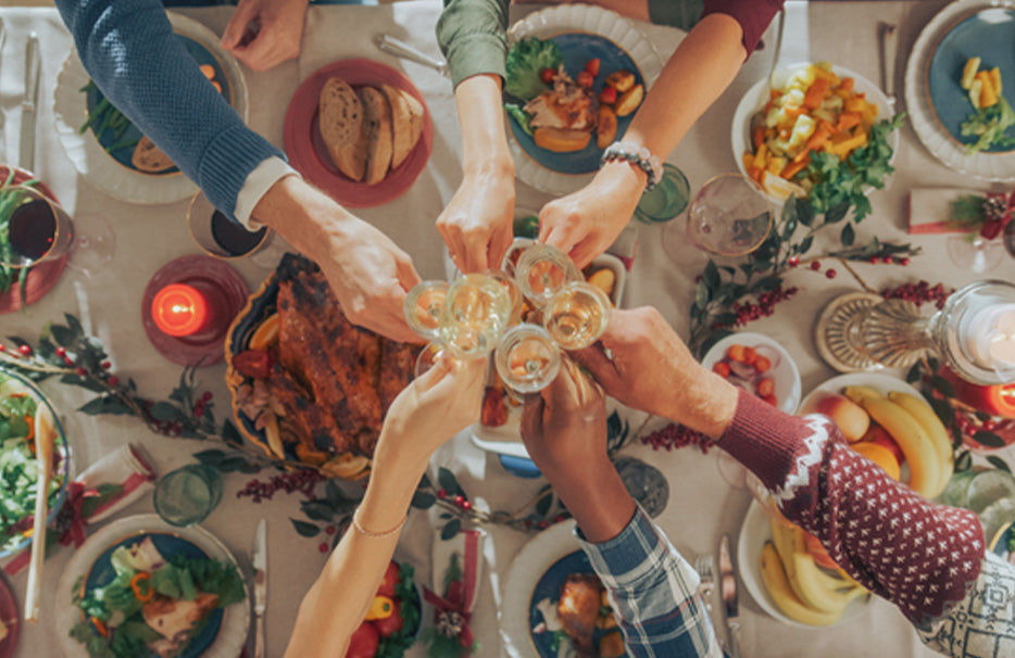 Festlich gedeckter winterlicher Tisch von oben, an dem mehrere Personen mit Gläsern anstoßen