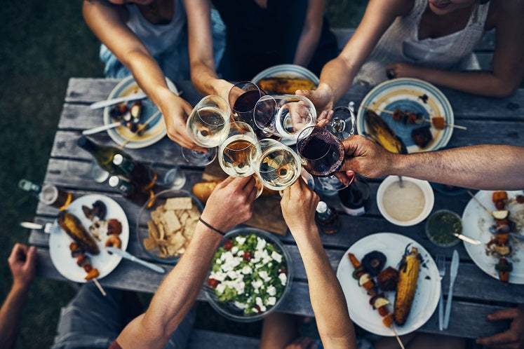 Mehrere Menschen stoßen an einem gedeckten Tisch gemeinsam mit Weingläsern an und genießen ein Essen zusammen.